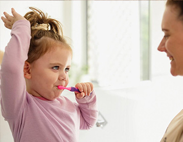 Toddler brushing her teeth while mom watches